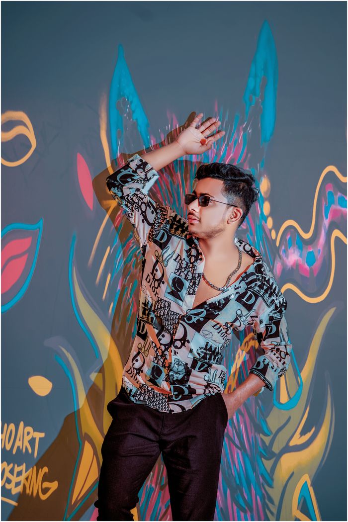 A fashionable man poses confidently against a colorful graffiti wall, wearing sunglasses.