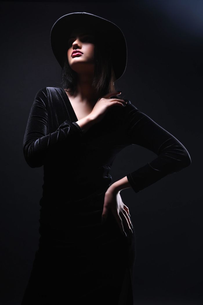 Artistic fashion portrait of a woman in a black velvet dress and hat, posing dramatically.