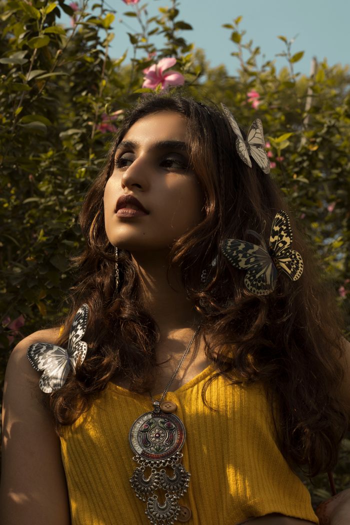 Portrait of a woman adorned with butterflies in a lush garden setting, exuding elegance and nature's beauty.